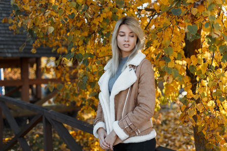 Cute attractive young girl blonde in stylish clothes walks in the park. Autumn, season, people concept - woman on a background of yellow autumn leavesの写真素材