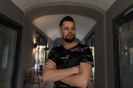 Confident hipster handsome young man with a stylish hairstyle and brutal beard in a military...