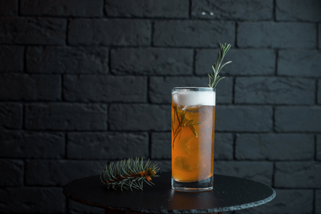 Golden unfiltered cold beer with white foam in a beer glass stands on a black wooden table in the bar. The drink is decorated with a spruce sprig. Served chilled. Enjoy the weekendの写真素材