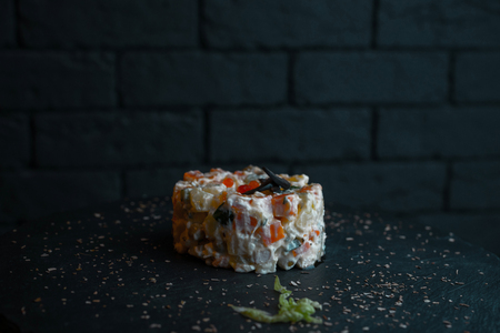 Traditional Russian delicious festive salad Olivier with sausage, with mayonnaise, with vegetables and boiled egg on a wooden table in a cafe. The original portion of food in the restaurant. New Year'の写真素材