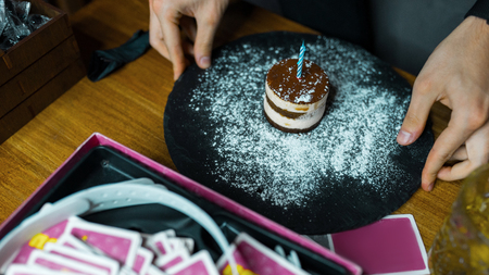 Birthday party in a cafe a festive sweet mini-cupcake with one candle decorated with icing sugar on the background of playing cards. Great weekend with friends. Happy Birthdayの写真素材