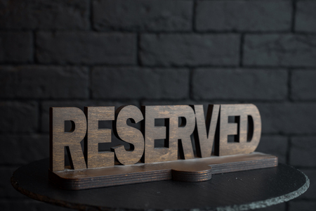 Vintage wooden carved figure Reserved on an empty black table in a restaurant against a black brick...