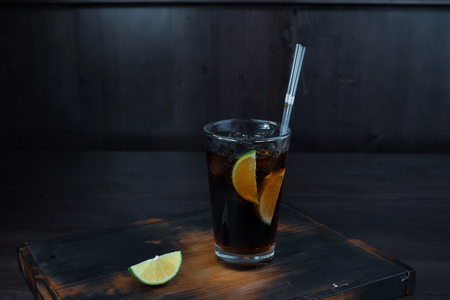 Alcoholic tasty cocktail with the addition of ice, whiskey and Coca-Cola, lime slices stands on a wooden table in the restaurant. The original serving of drinks in the bar.の写真素材