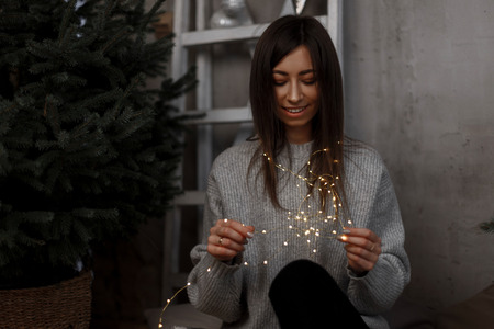 Beautiful young woman is smiling and holding a bright garland in festive New Year's room. Magical Christmas atmosphere. Positive girlの写真素材