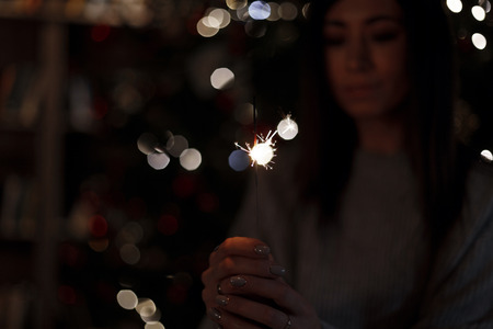 Young beautiful woman holds in hand a sparklers in a dark room with light.の写真素材