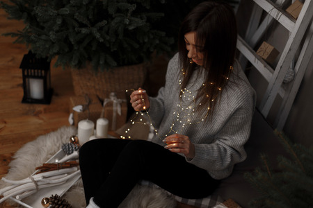 Attractive young woman in knitted clothes with fabulous lights dreaming and sitting on the floor in the Christmas room. Nice girl smiling. View from aboveの写真素材
