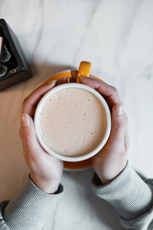 Female hands hold a cup with delicious coffee with cream on the background of a vintage table in a cafe. Morning coffee break. Close-up. View from above.の写真素材