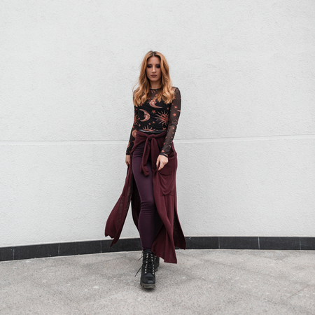Beautiful red-haired young woman in a fashionable blouse in a pattern in pants in boots with a purple cape goes on the background of a white building. Pretty attractive girl model for a walk. Style.の写真素材