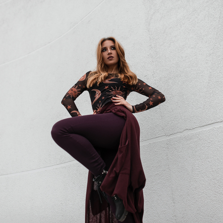 Fashionable pretty attractive young red-haired woman in stylish clothes posing outdoors near a white building on a spring day. European urban girl fashion model on a walk. Youth style women's clothingの写真素材