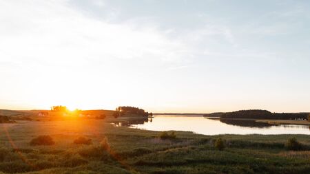 Summer landscape with lake in the field with blue sky. Sunset orange sun on the horizon.の写真素材