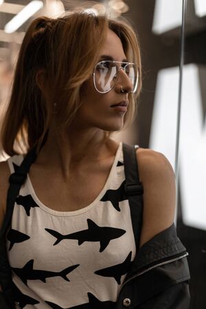 Portrait of a pretty young hipster woman in vintage glasses with an earring in nose with a trendy...