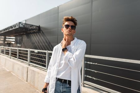 European stylish young hipster man in fashionable summer clothes in black sunglasses with a...