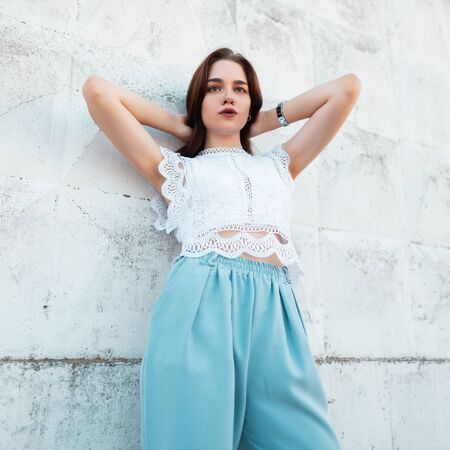 Pretty modern young model woman in a elegance lace blouse in fashionable blue pants poses near a...