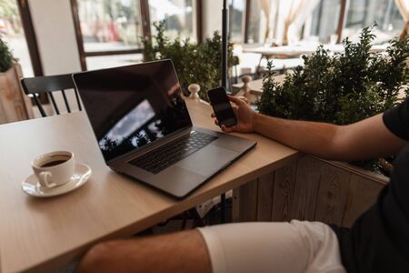 Young professional businessman sits in a cafe at a table with a phone in  hand. Close-up of a...
