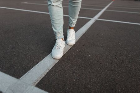 Trendy young man in vintage white leather sneakers in fashionable blue denim pants. Stylish men's summer shoes. Casual design. Close-up of male legs.の写真素材