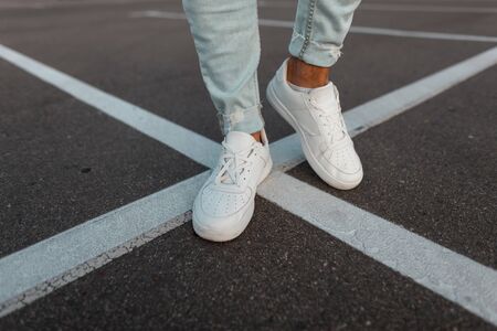 Close-up of male legs. Fashionable young man stands on the asphalt road in leather stylish white...