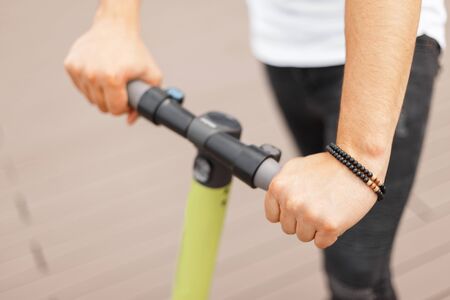 Young man is holding the steering wheel of an electric scooter. Guy with a modern scooter. Close-up...