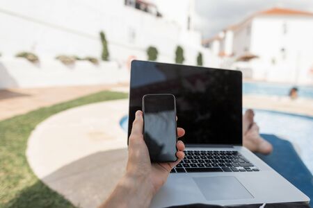 Young designer man with a phone in his hands and with a laptop is resting after a hard day at the...