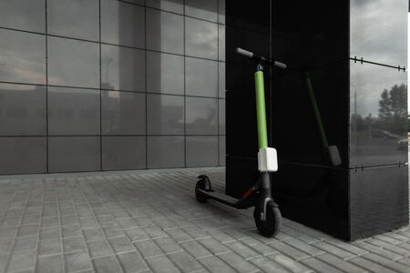 Yellow-black electric scooter stands on a street in a city near a black building. Modern transport.