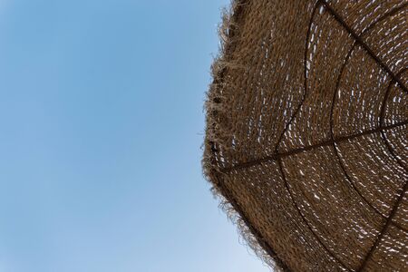 Beach umbrella made of straw on a background of blue sky. Summer photo. Sunny day.