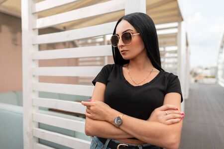 Pretty urban young woman fashion model with luxurious black hair in trendy black t-shirt in stylish...