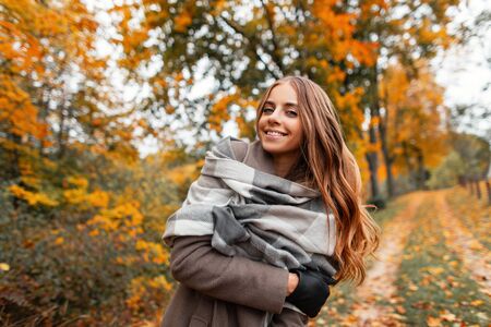 Young cute modern cheerful woman in a vintage knitted scarf in a warm autumn coat poses and smiling...