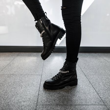 Young modern woman in black stylish jeans in fashionable leather lace-up boots stands in a store....