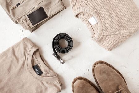 Fashionable black leather belt with a metal buckle on a table among fashionable men's clothing in beige colors. Closeup of a sweater with pants with a pullover with boots with a belt on a white table.の写真素材