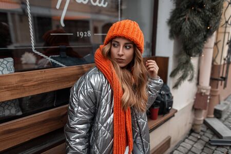 Red-haired young woman in a stylish knitted hat with an orange trendy scarf in a fashionable shiny...