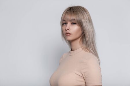 Stylish portrait of a young blonde woman in a fashionable beige t-shirt on a white wall background...