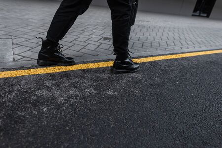 Close up of male stylish legs in trendy leather boots in black trendy jeans on the asphalt in the city. Modern guy in vintage shoes is walking on the road.New autumn-spring footwear collection for menの写真素材