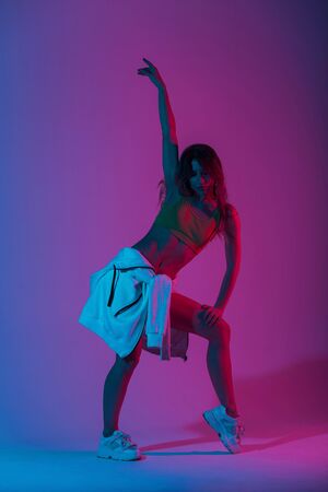 Modern young woman dancer in fashionable youth clothes in a white sneakers dancing in a room with blue light. Sexy pretty beautiful girl model enjoys a dance in the studio with neon amazing color.の写真素材