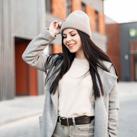 Happy portrait beautiful pretty young woman with cute smile with black long hair in fashionable youth clothes outdoors. Cheerful stylish girl model is walking and smiling on spring day. Street fashionの写真素材