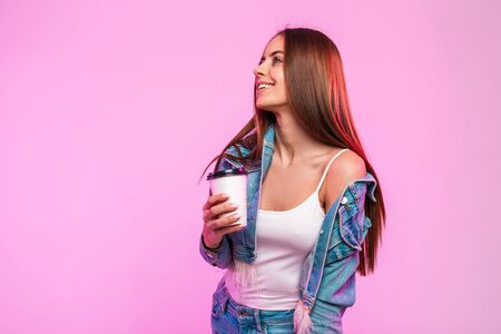 Funny stylish young woman in trendy blue denim jacket in vintage white t-shirt with cup of tasty...