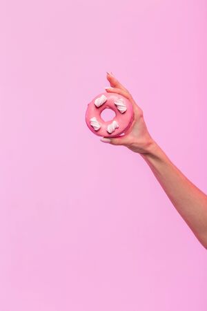 Female hand holds tasty colored donut on pink background. Sweets, dessert, concept- not healthy food. Close-up.の写真素材