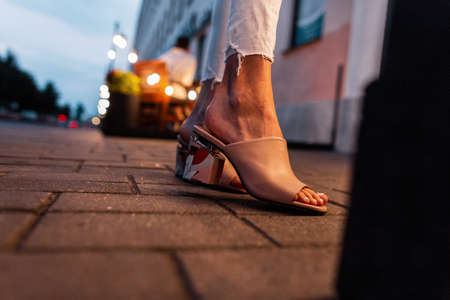 Fashionable girl in stylish beige summer shoes stands on a tile in the city in the evening, close up.の写真素材