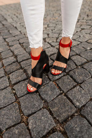 Fashionable female legs in stylish shoes and white jeans stands on a stone road in the city....