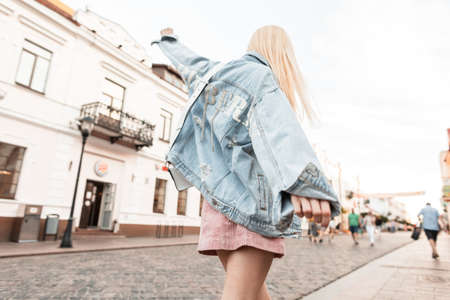 Fashion woman in a denim jacket in a pink dress walks and keeps balance on the street.の写真素材