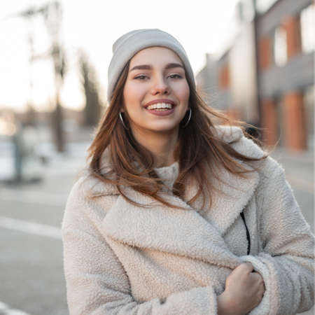 Portrait of a happy attractive young woman with a beautiful smile in a trendy faux fur coat in a...