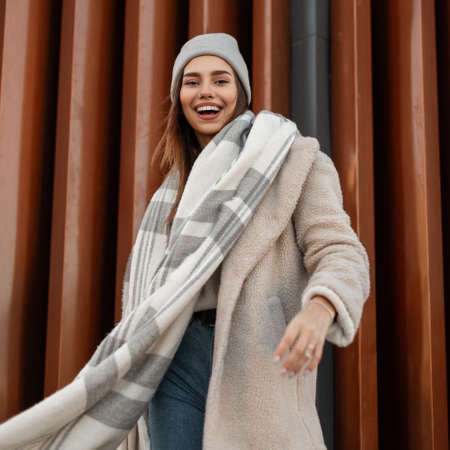 Cheerful girl with funny smile in trendy clothes outdoors. Positive young woman in coat in a knitted...