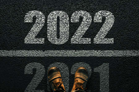 Men's feet in boots on the pavement 2021 and go into 2022. New Year's 2022 Concept. White numbers 2022 on asphalt, top viewの写真素材