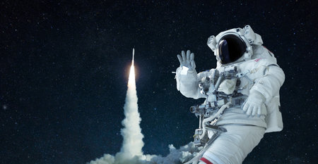 Space man in a space suit and hat travels in open space and waves his hand against the background of a rocket lift off. Spaceship takes off successfully. Welcome to space, conceptの写真素材