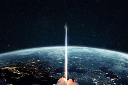 Successful launch of a rocket from planet Earth into outer space. Space shuttle takes off into starry cosmos with the planet earth with night city lights. Spaceship lift off conceptの写真素材