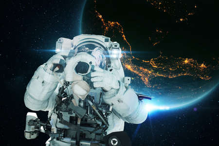 Spaceman astronaut with a camera takes a photo in open space with the blue planet earth and the lights of night cities. Space mission and space photographer conceptの写真素材