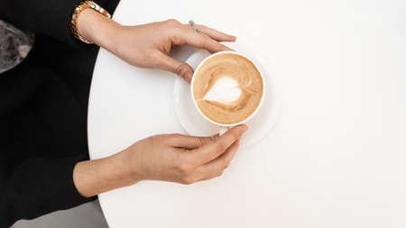 Young woman holding a cup with hot coffee in the cafe. Girl is sitting in the morning in the...