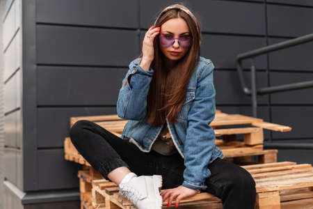 European beautiful young hipster woman in fashionable violet glasses in stylish denim jacket in...