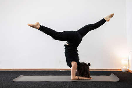 Young woman does handstand and keeps balance in a fitness room. Girl is standing in a yoga pose and...