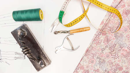 Workspace top view with sewing kit. Threads, centimeter, fabric, press, scissors and sketch on the...
