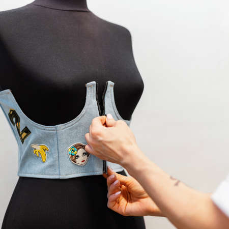 Female hands wear a stylish denim vest on a black mannequin. Concept of working as a fashion designer in a studioの写真素材