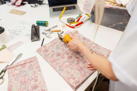 Tailor seamstress girl with electric cutter cuts fabric in studio